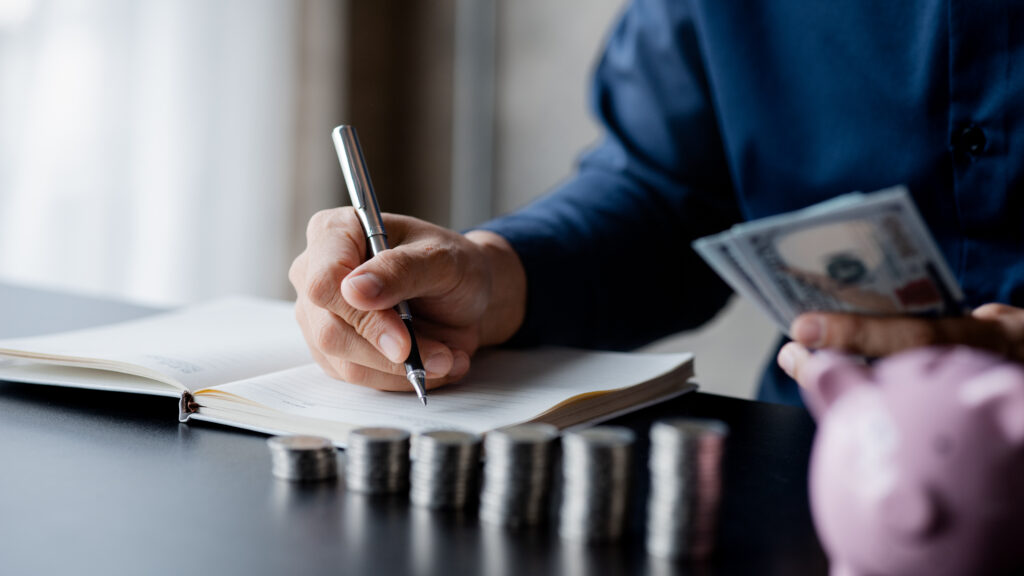 man writing a budget while holding money