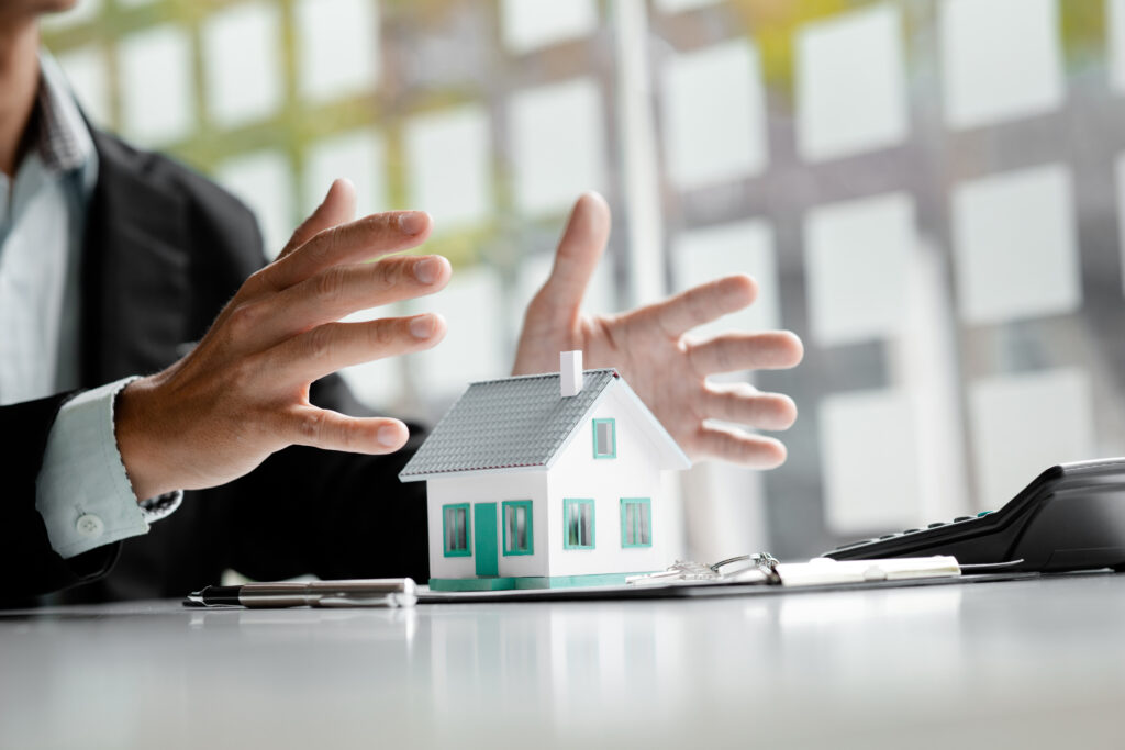 Person covers the model with his hand, Insurance house, and family health live concept. The insurance agent presents the hands protection model that symbolize the coverage.