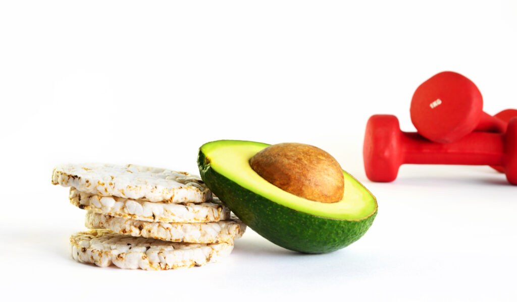 4 rice cakes with half an avocado leaning on them with 2 red dumbbells in the background