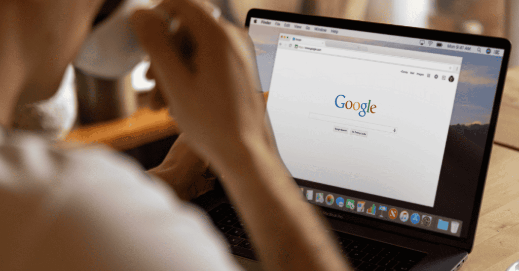 A person sips coffee while using a laptop displaying the Google homepage, indicating a search or SEO-related activity.