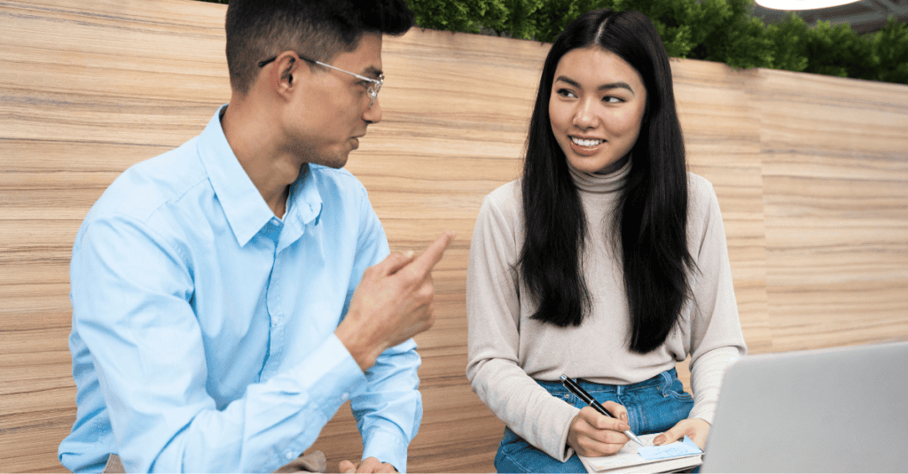 A man and woman having a collaborative affiliate discussion while reviewing notes on a laptop.