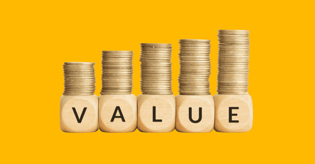 Wooden blocks spelling out “VALUE” with increasing stacks of gold coins on top, symbolizing growth in financial or perceived value.