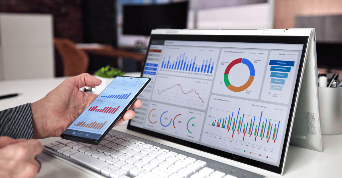 A person analyzes marketing campaign performance using data dashboards displayed on a smartphone and a foldable laptop screen, featuring various charts, graphs, and KPIs.