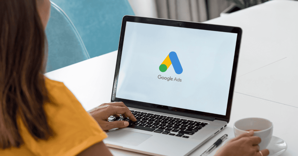 A woman working on a laptop with the Google Ads logo on the screen, indicating setup or management of a PPC campaign.